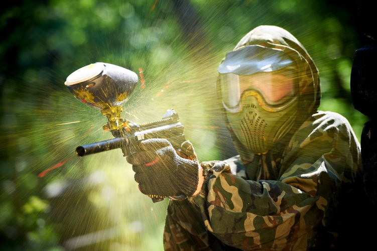 paintball sport player wearing protective mask aiming gun and shotted down with paint splash in summer